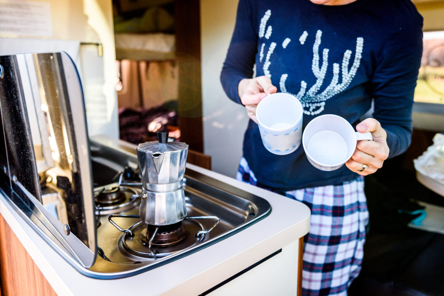 Cooking coffee in campervan, caravan or RV on camping trip. Woman is making coffee in the morning using italian kafetiera on a family vacation camping trip.